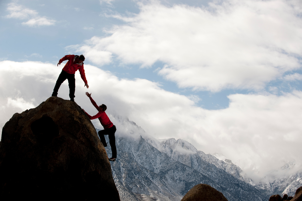 Man on top of mountain helping someone up